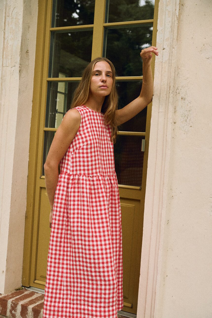 Woman wearing a sleeveless red and white gingham linen dress with a gathered, midi-length skirt.